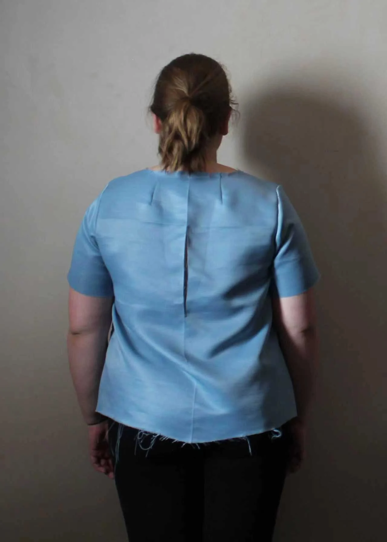 Back view of a woman wearing a blue development sample with visible fitting seams.