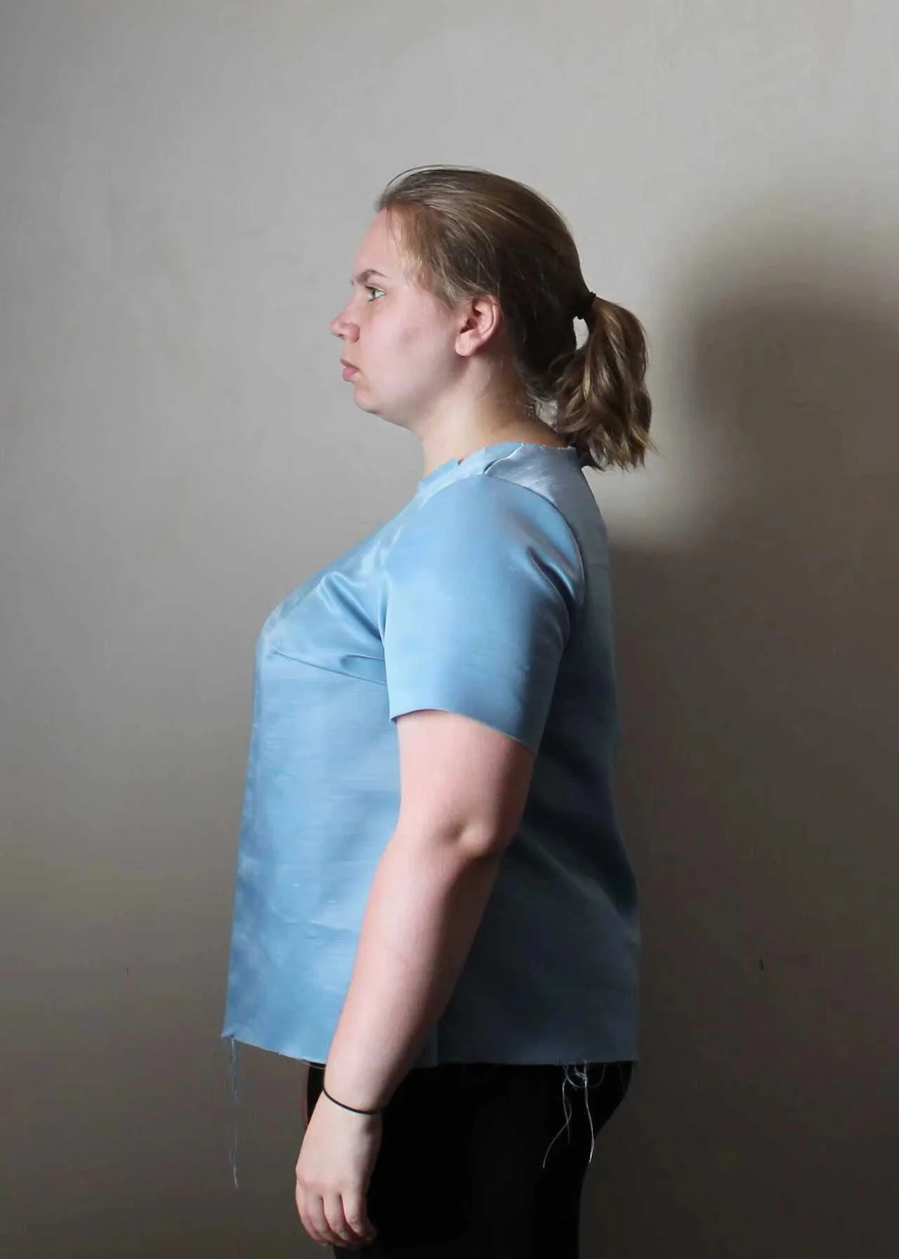 Side view of a woman wearing a blue development sample with visible fitting seams.