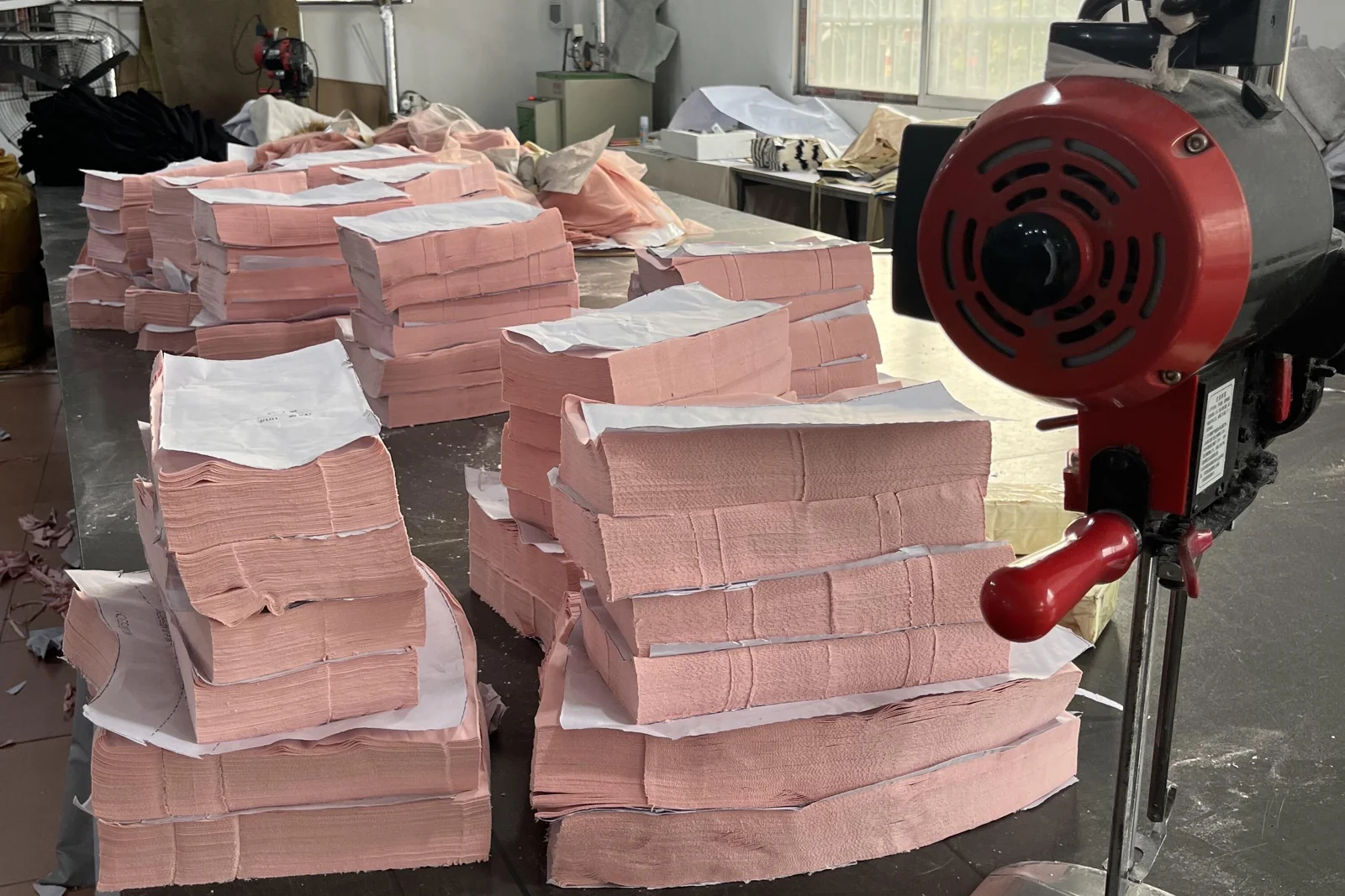 Stacked pink fabric components beside upright cutting equipment.