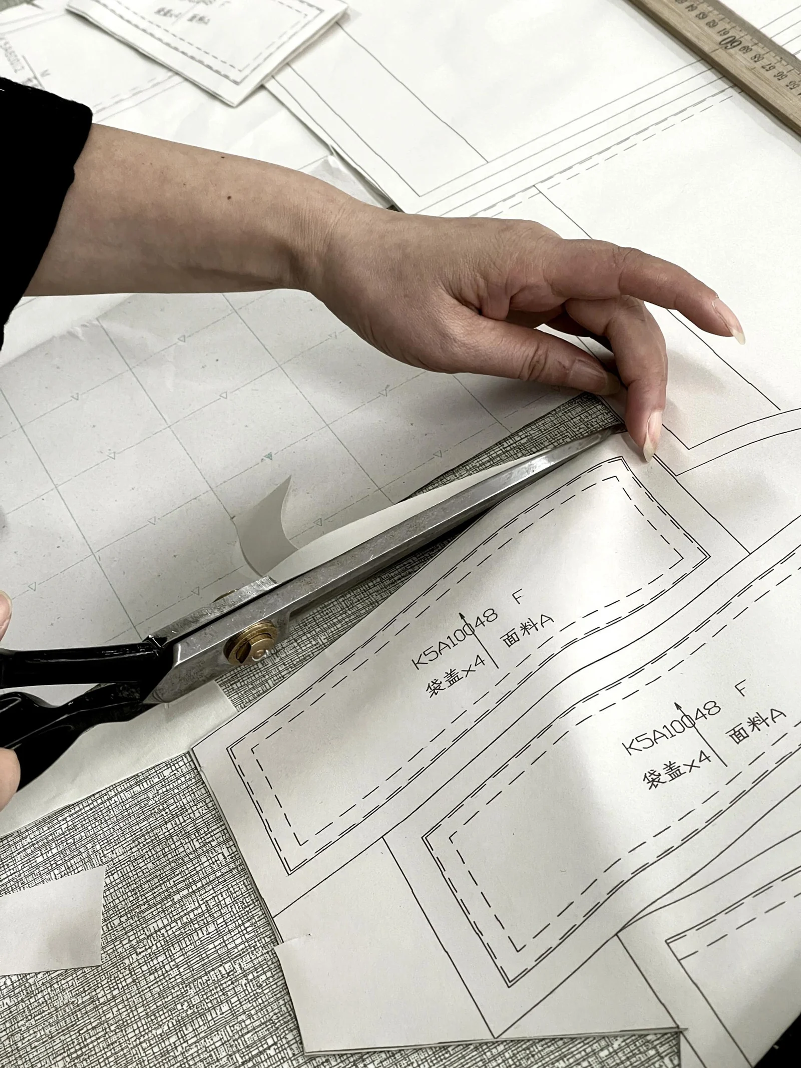 Hands cutting a paper garment pattern with shears.