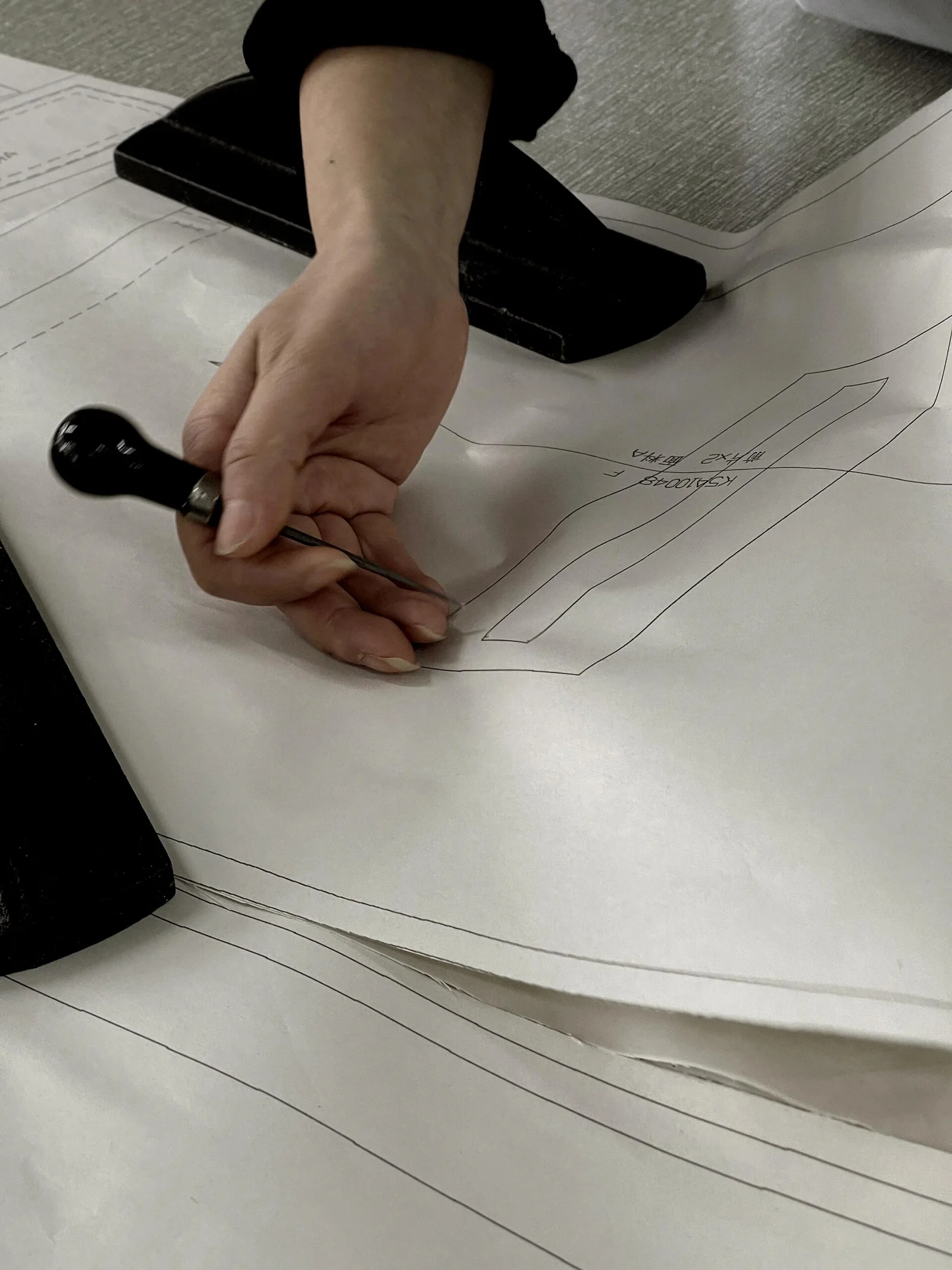 A hand working on a printed paper garment pattern.