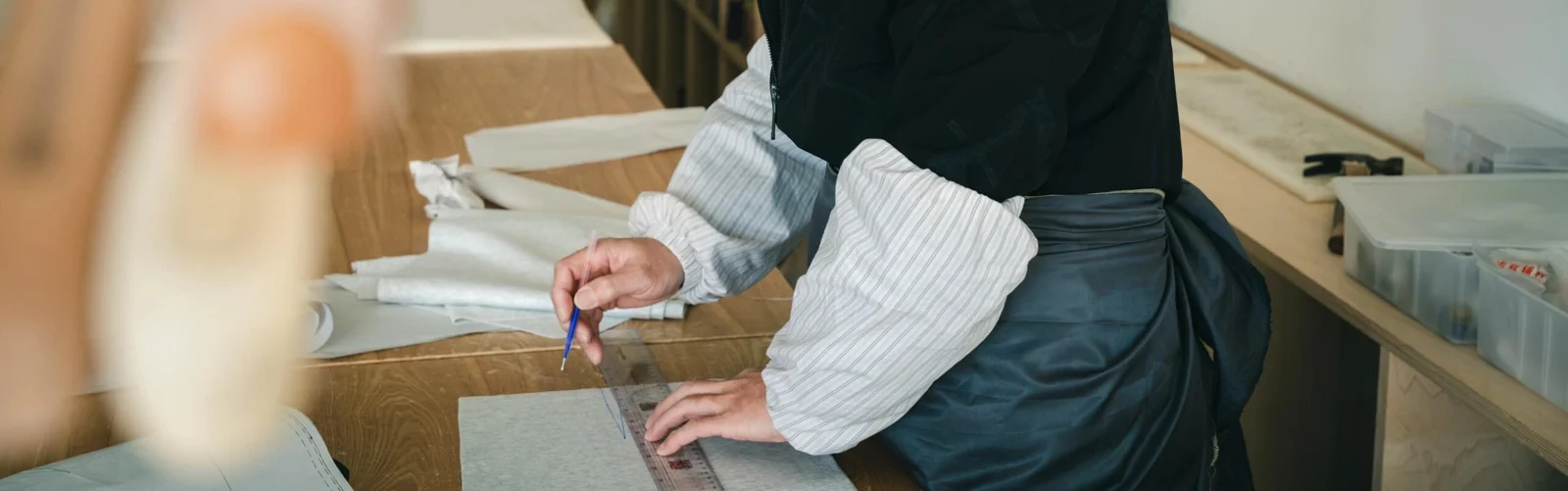Hands marking a garment pattern with a ruler on a worktable.