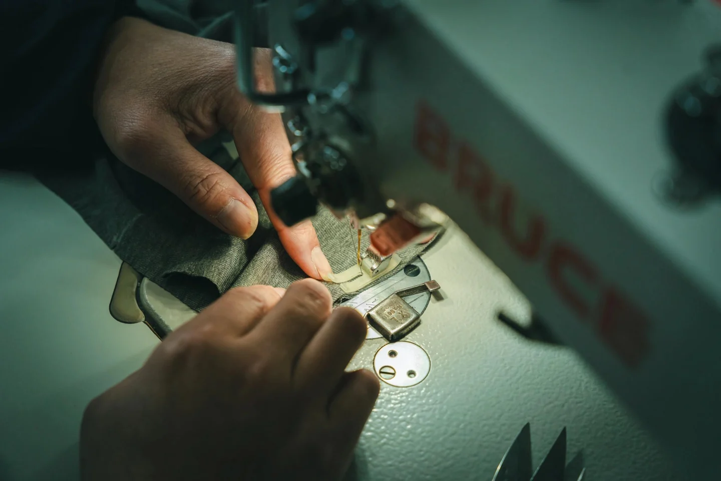 Hands guiding fabric under an industrial sewing-machine needle.