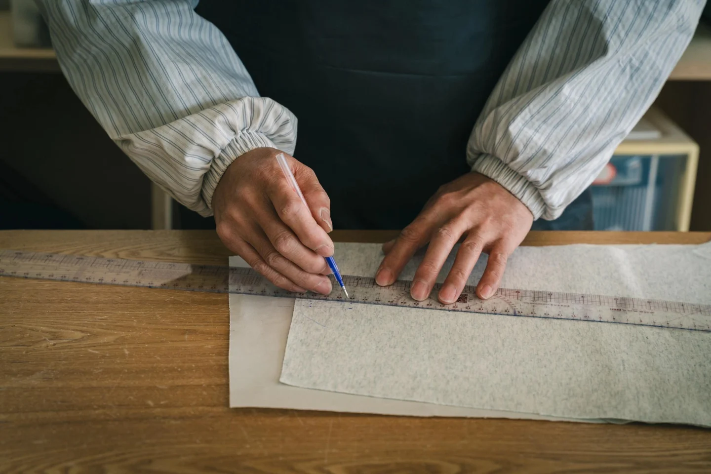 Hands using a ruler to measure and mark a paper garment pattern.