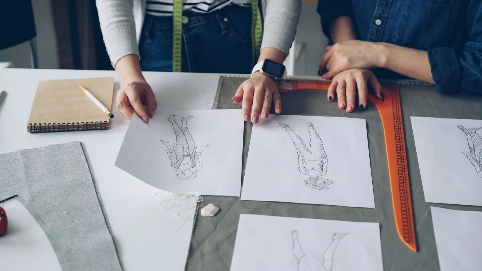 Hands reviewing garment drawings and fabric references.