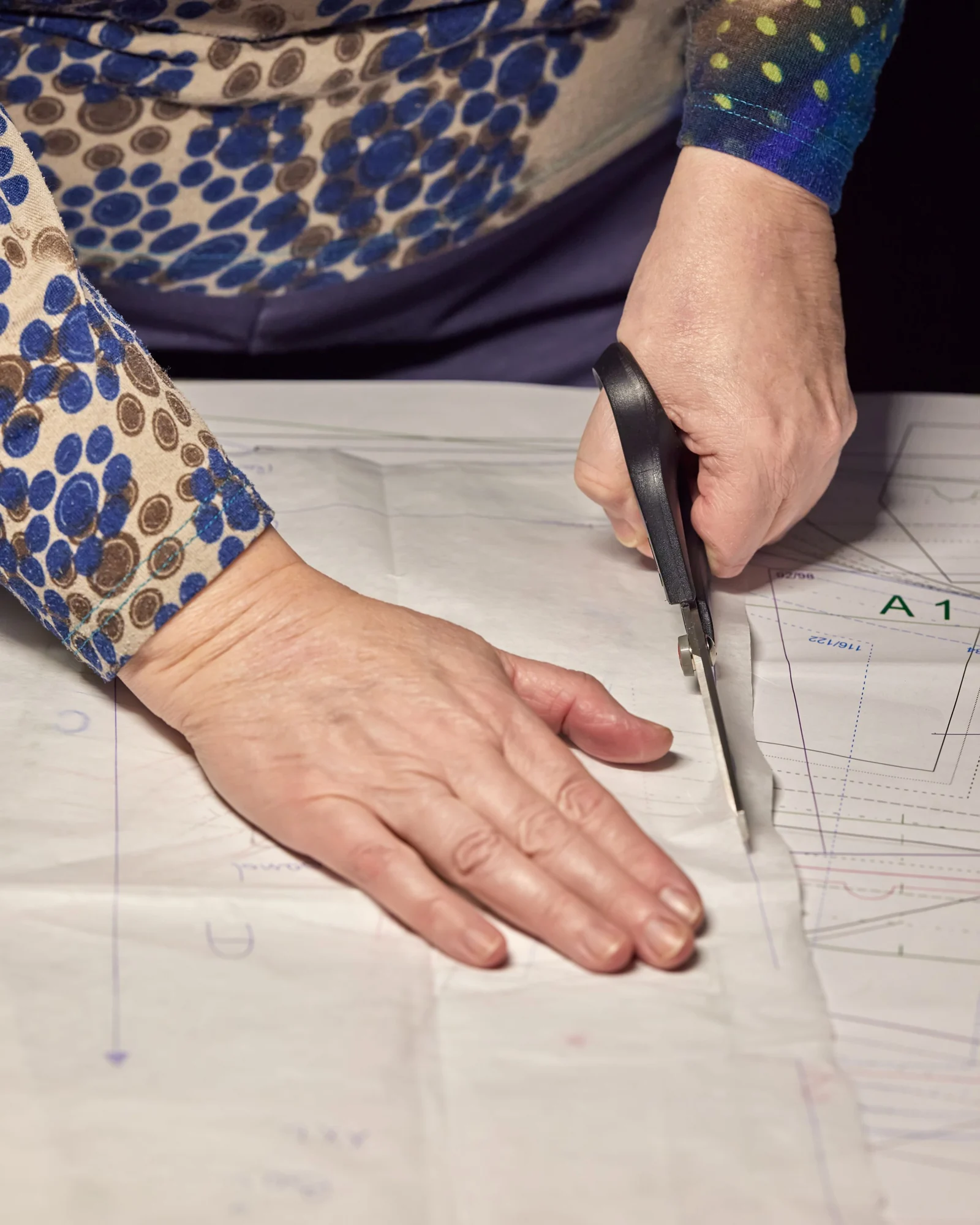Hands cutting a paper garment pattern with shears.