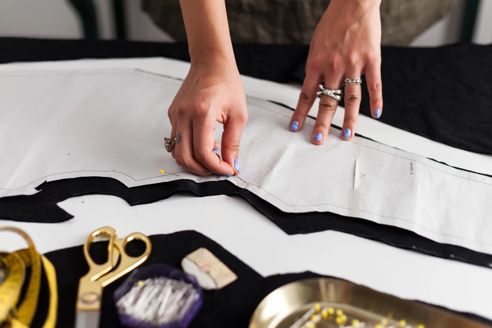 Hands pinning a paper pattern to dark fabric.